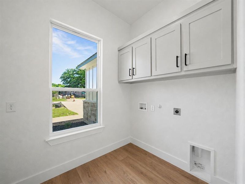 Utility space featuring wood-finish flooring, white walls, and built-in white shaker-style cabinetry with black hardware Utility space featuring wood-finish flooring, white walls, and built-in white shaker-style cabinetry with black hardware