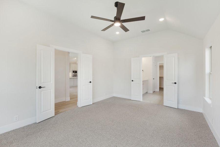 Empty bedroom with carpet, ceiling fan, vaulted ceiling, and doors leading to bathroom and walk-in closet
