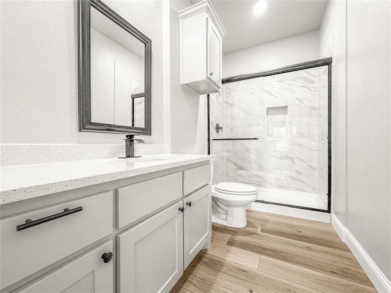 Modern bathroom featuring a vanity with a white speckled countertop, dark fixtures, and wood-finish flooring Modern bathroom featuring a vanity with a white speckled countertop, dark fixtures, and wood-finish flooring