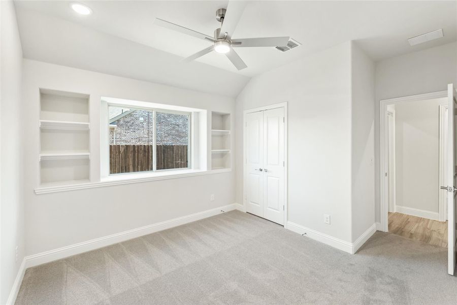 Empty bedroom with vaulted ceiling, ceiling fan, built-in shelves, and carpeted floor