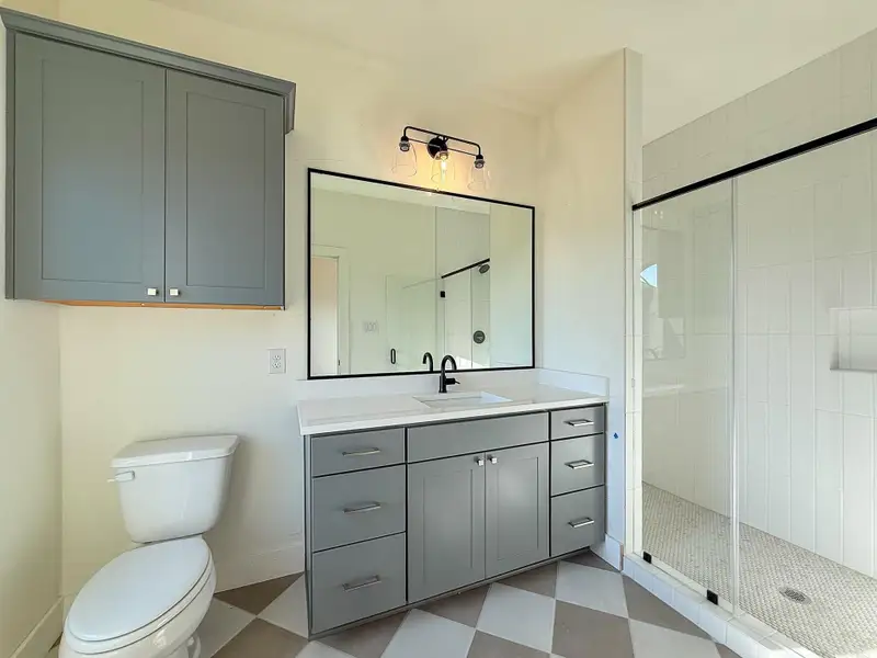 One of the secondary bathrooms with a beautiful floor-to-ceiling tiled glass-enclosed shower with ample vanity space and storage.