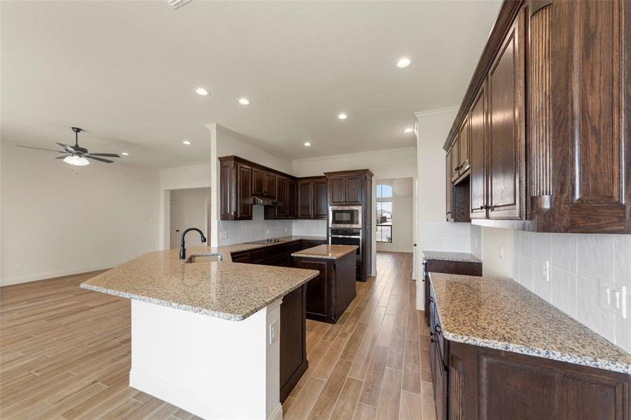 Kitchen featuring dark wood finish cabinets, backsplash, wood finish floors, light stone countertops, and a peninsula Kitchen featuring dark wood finish cabinets, backsplash, wood finish floors, light stone countertops, and a peninsula