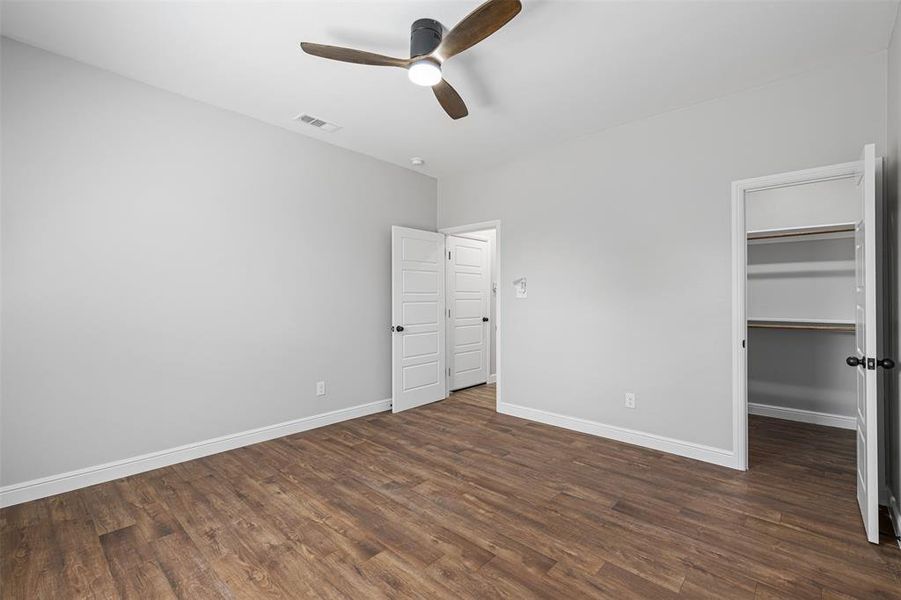 Unfurnished bedroom with ceiling fan, a walk in closet, a closet, and dark hardwood / wood-style flooring