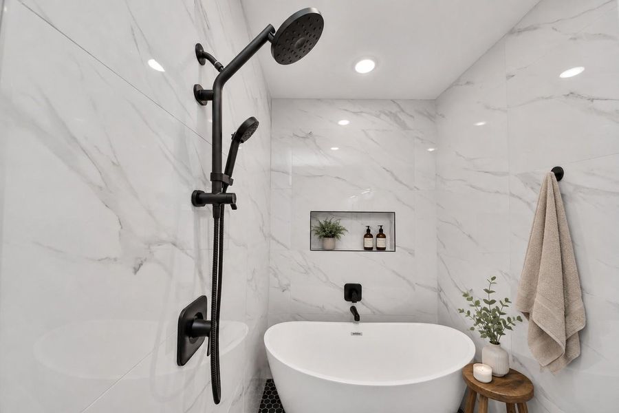 Elegant freestanding soaking tub surrounded by floor-to-ceiling marble-look tile, creating a serene spa-inspired retreat.