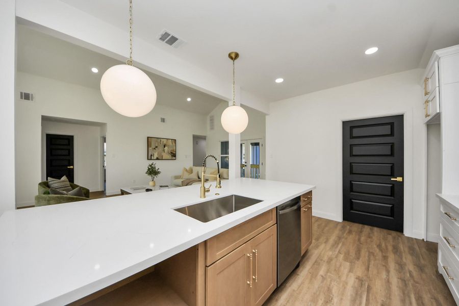This modern kitchen features a spacious white quartz island with a built-in sink, stylish pendant lighting, and sleek cabinetry. The open layout flows into a cozy living area with wood flooring and contemporary decor. This modern kitchen features a spacious white quartz island with a built-in sink, stylish pendant lighting, and sleek cabinetry. The open layout flows into a cozy living area with wood flooring and contemporary decor.