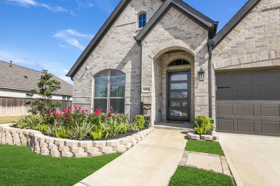 This photo showcases a modern brick home with a welcoming front entrance. It features a well-maintained garden with vibrant flowers and greenery, a clean walkway, and a contemporary garage door. The arched window and door add architectural interest.
