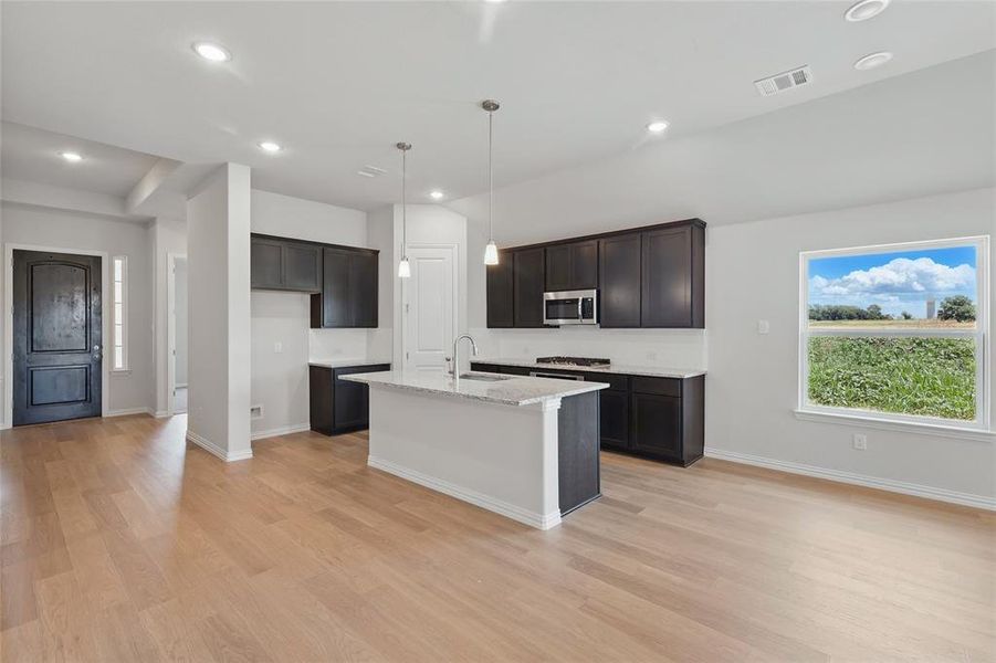 Kitchen with stainless steel microwave, a sink, light wood-style floors, an island with sink, and recessed lighting