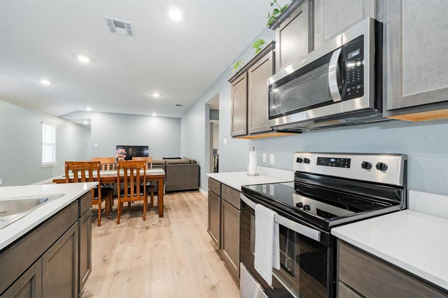 Kitchen featuring appliances with stainless steel finishes, light wood finished floors, recessed lighting, open floor plan, and dark brown cabinets Kitchen featuring appliances with stainless steel finishes, light wood finished floors, recessed lighting, open floor plan, and dark brown cabinets