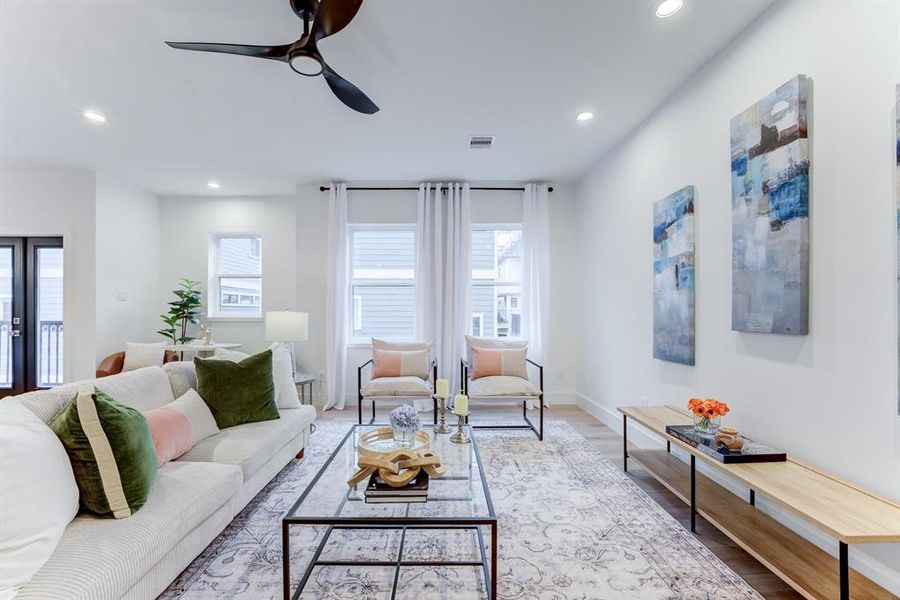 This spacious living room features an open layout with light wood flooring, modern decor, and ample natural light from large windows and double door balcony.