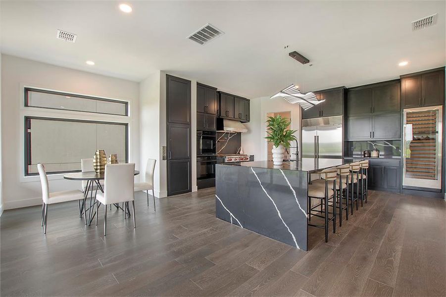 Kitchen featuring double oven, dark wood-type flooring, a center island with sink, and built in fridge