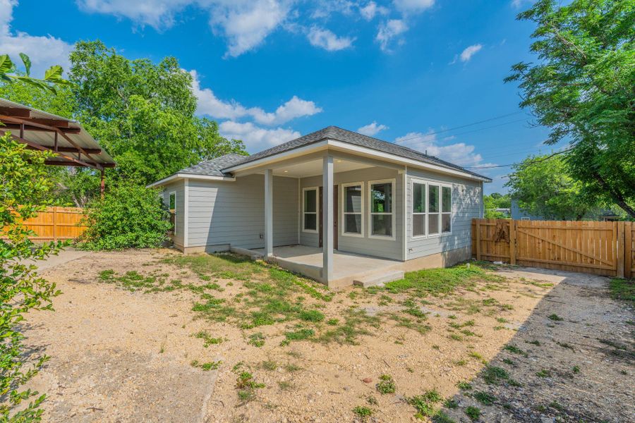 Rear exterior featuring gray siding, a covered patio, multiple windows, a wood fence, and mature trees