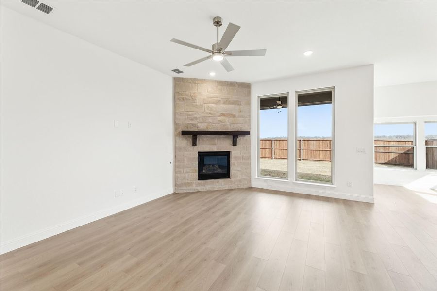 Open living room with stone corner fireplace, ceiling fan, and light hardwood floors Open living room with stone corner fireplace, ceiling fan, and light hardwood floors
