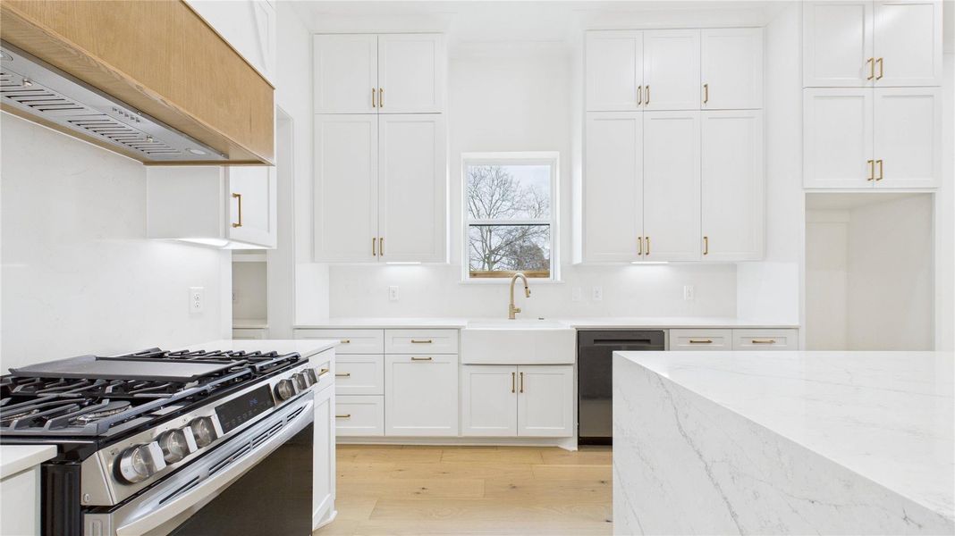 This kitchen features a modern design with white cabinetry, a premium LG stove with air fryer and convection, and a farmhouse sink. It includes a sleek quartz countertop and ample storage, gold fixtures and is illuminated by natural light from a central window.