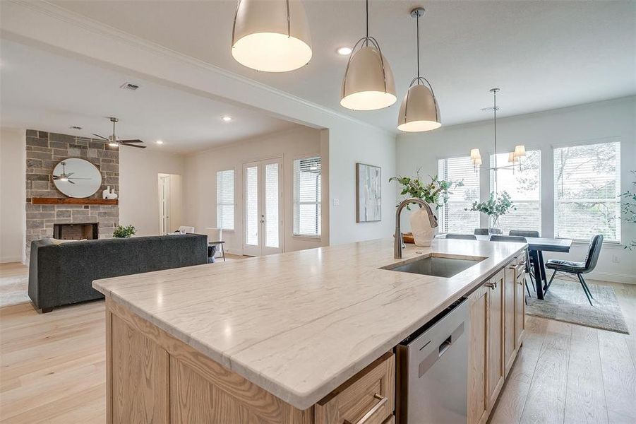 Kitchen featuring light hardwood flooring, a kitchen island with leathered Quartzite countertops, farm sink, natural stain custom cabinetry with soft close drawers and cabinets.