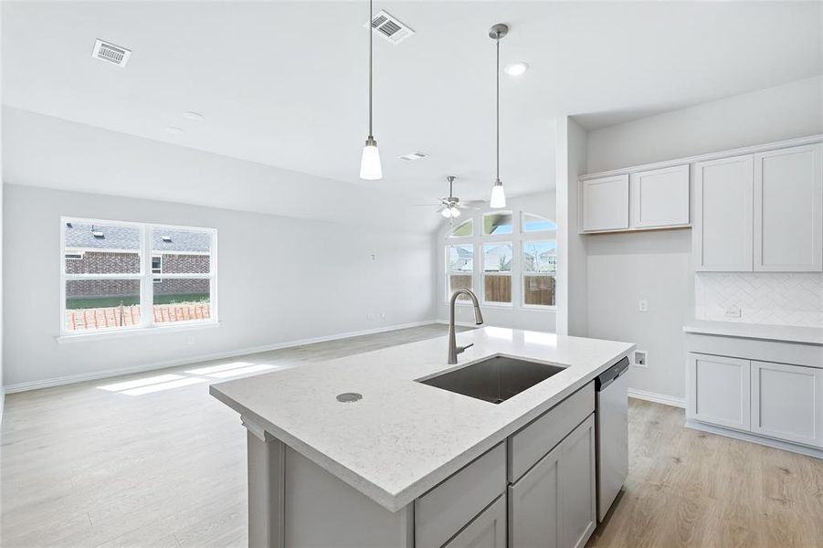 Kitchen featuring light wood finished floors, decorative light fixtures, decorative backsplash, ceiling fan, and a kitchen island with sink Kitchen featuring light wood finished floors, decorative light fixtures, decorative backsplash, ceiling fan, and a kitchen island with sink
