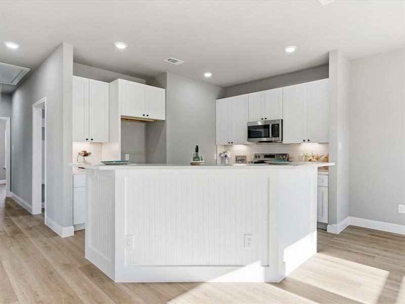 Kitchen with white cabinets, light countertops, decorative backsplash, appliances with stainless steel finishes, and a kitchen island with sink Kitchen with white cabinets, light countertops, decorative backsplash, appliances with stainless steel finishes, and a kitchen island with sink