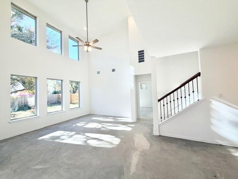 Unfurnished living room featuring unfinished concrete floors, ceiling fan, and a towering ceiling