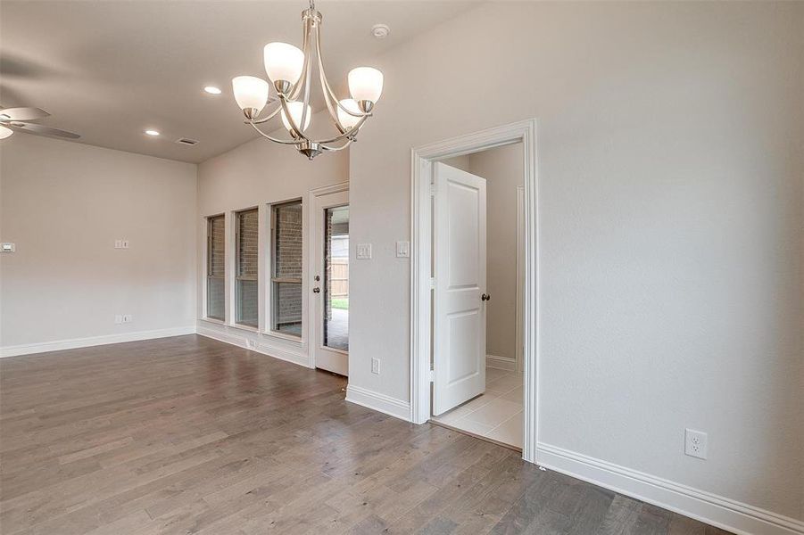 Empty room with ceiling fan with notable chandelier and light hardwood / wood-style floors