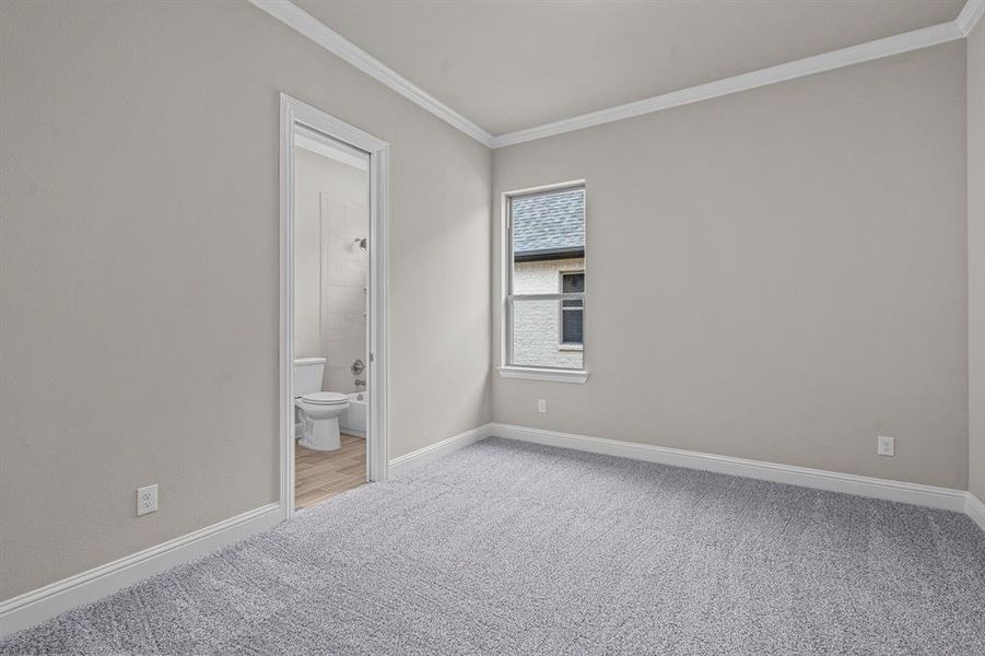 Unfurnished bedroom with crown molding, connected bathroom, and carpet floors Not actual home. Previous built example.