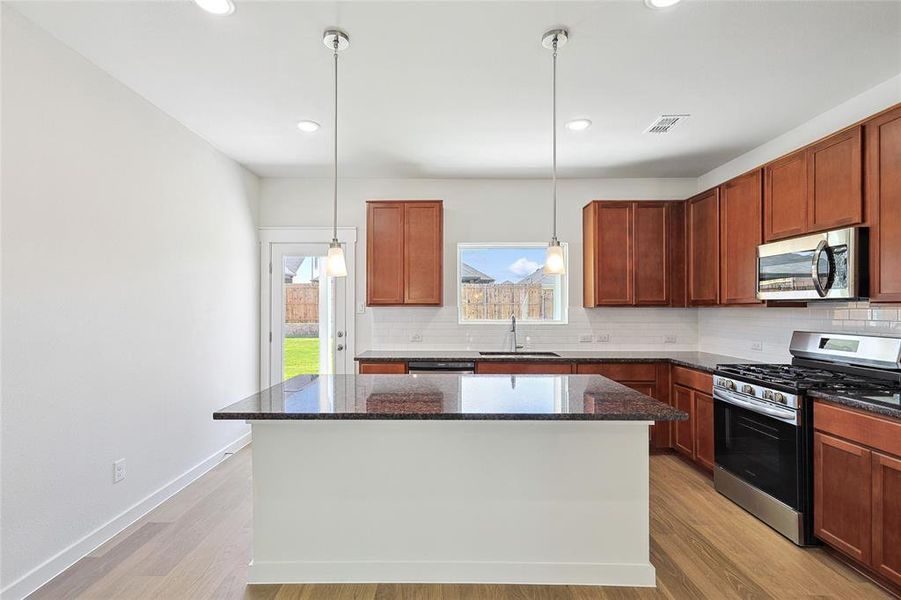 Kitchen featuring hanging light fixtures, light hardwood / wood-style floors, a kitchen island, stainless steel appliances, and sink