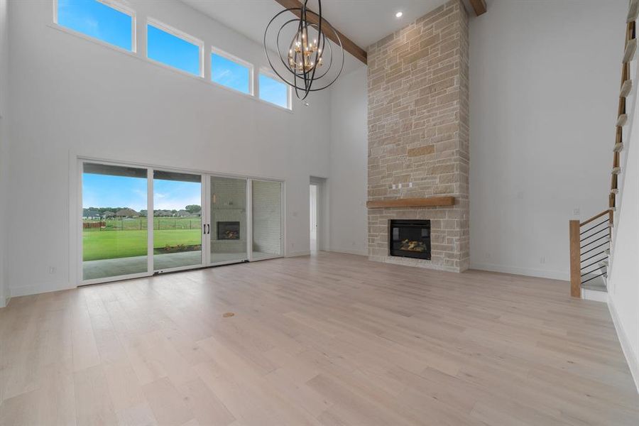 Unfurnished living room featuring an inviting chandelier, light hardwood / wood-style flooring, a fireplace, and a high ceiling