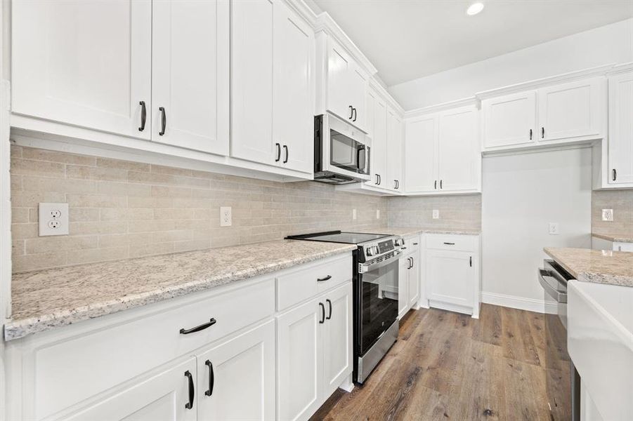 Kitchen with white cabinetry, hardwood / wood-style floors, appliances with stainless steel finishes, and tasteful backsplash