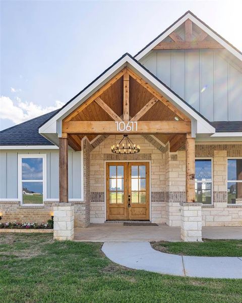 View of exterior entry featuring board and batten siding, french doors, stone siding, a shingled roof, and a lawn View of exterior entry featuring board and batten siding, french doors, stone siding, a shingled roof, and a lawn