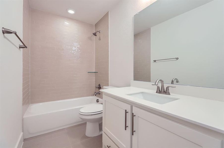 Full bathroom with tile patterned floors, vanity, tiled shower / bath combo, and toilet