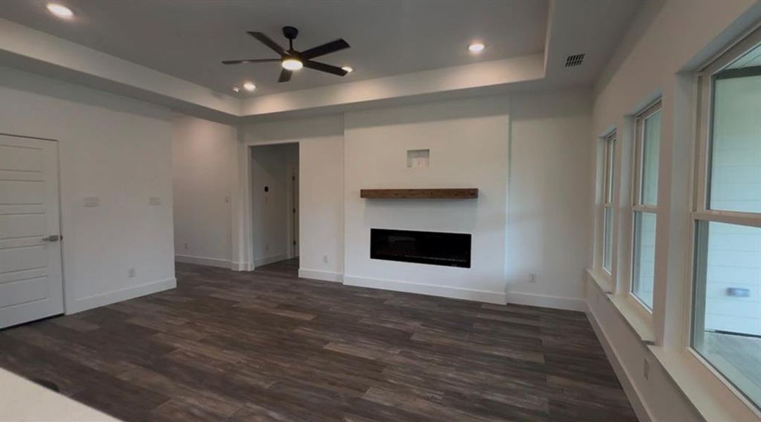 Spacious living area featuring a modern linear fireplace with a wood mantel, wood-finish flooring, recessed lighting, a ceiling fan, and multiple windows