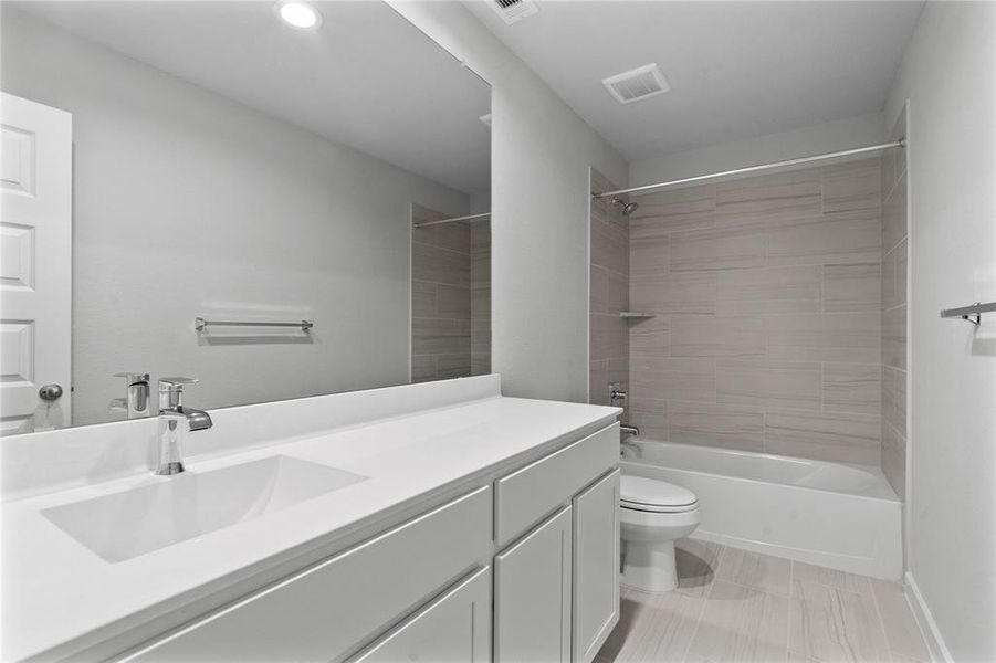 Secondary bath features tile flooring, bath/shower combo with tile surround, stained wood cabinets, beautiful light countertops, mirror, sleek fixtures and modern finishes.