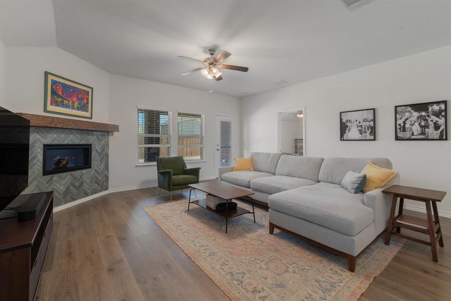 Living area with ceiling fan, wood finished floors, baseboards, vaulted ceiling, and a tiled fireplace