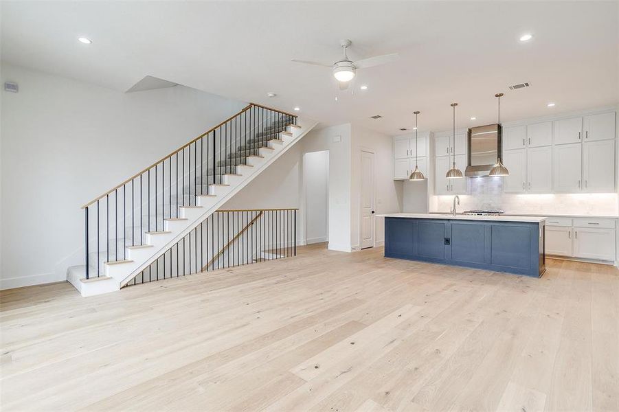 Kitchen with light wood finished floors, light countertops, white cabinets, pendant lighting, and wall chimney exhaust hood