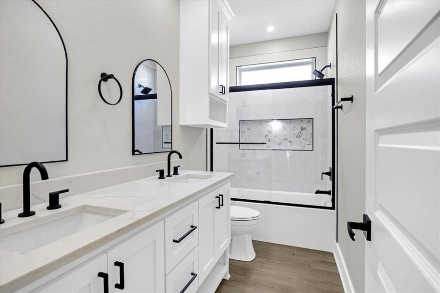Bathroom featuring bath / shower combo with glass door, double vanity, and light wood-style flooring