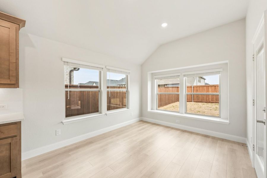 Empty dining area with vaulted ceiling, light wood floors, and large windows overlooking backyard fence Empty dining area with vaulted ceiling, light wood floors, and large windows overlooking backyard fence
