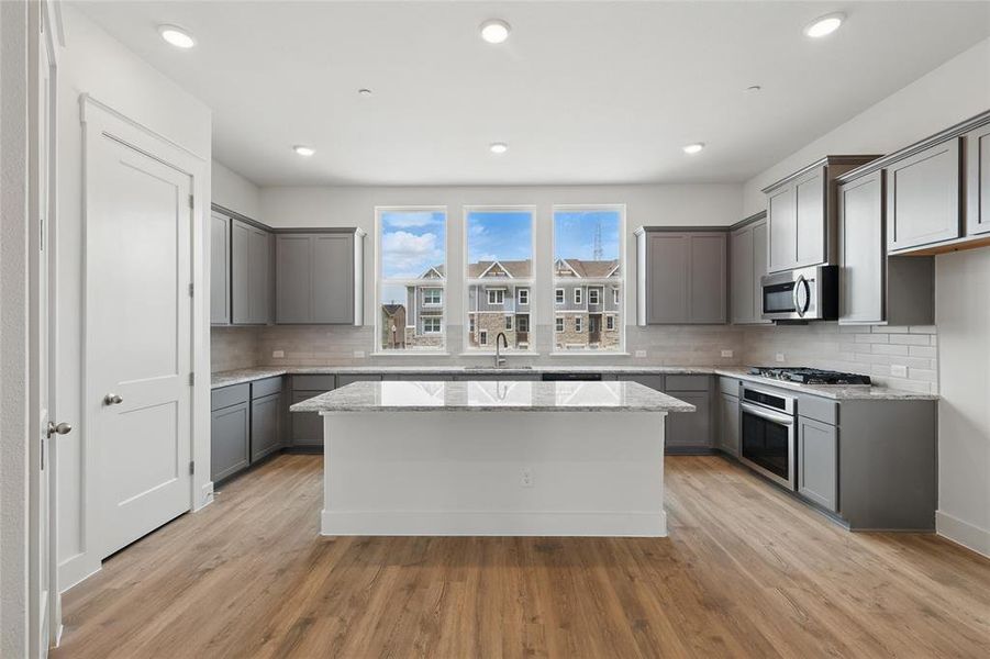 Kitchen with gray cabinetry, light stone counters, a kitchen island, and recessed lighting
