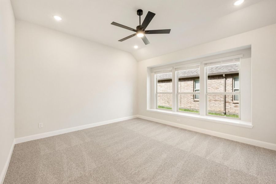 Empty bedroom with carpet flooring, ceiling fan, and triple window with natural light