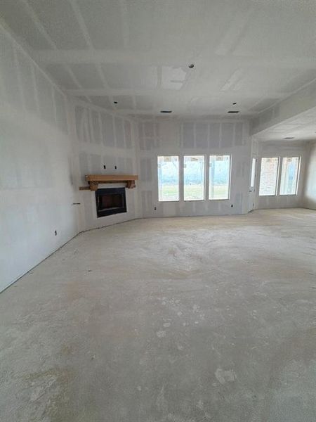 Unfurnished living room featuring a fireplace and unfinished concrete flooring Unfurnished living room featuring a fireplace and unfinished concrete flooring