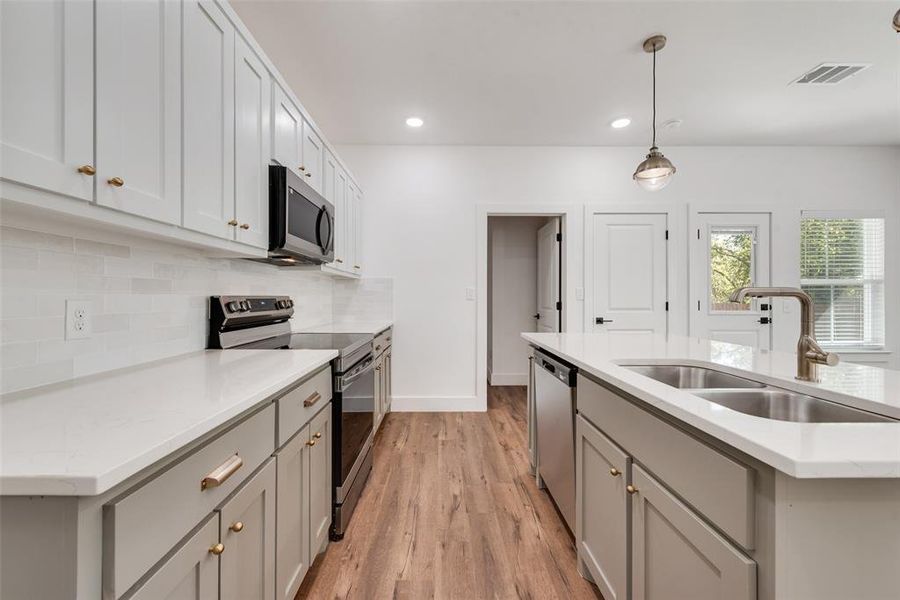 Kitchen with gray cabinetry, appliances with stainless steel finishes, pendant lighting, light wood finished floors, and tasteful backsplash Kitchen with gray cabinetry, appliances with stainless steel finishes, pendant lighting, light wood finished floors, and tasteful backsplash