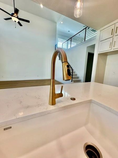 A stylish kitchen sink with a golden faucet and white countertops overlooks a lofty living area with a ceiling fan.