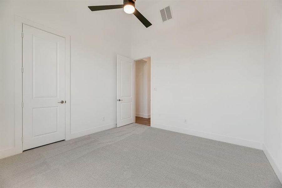 Unfurnished bedroom with light colored carpet, a ceiling fan, and a towering ceiling