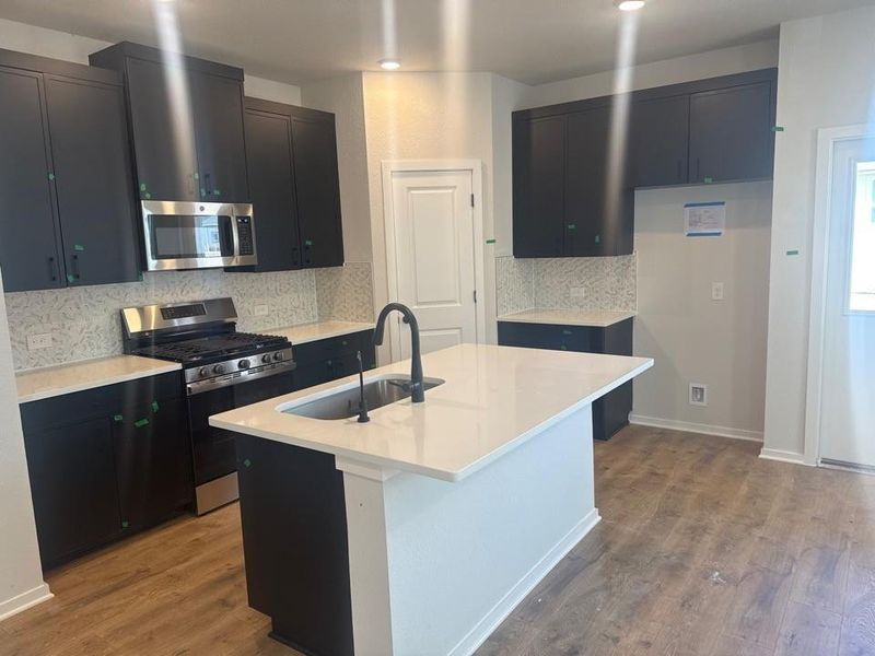 Kitchen featuring dark cabinets, stainless steel appliances, light stone counters, and backsplash