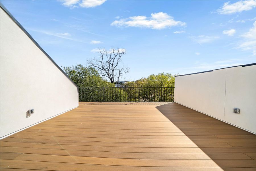 Expansive outdoor deck featuring wood-finish flooring, white stucco walls, and a black metal railing Expansive outdoor deck featuring wood-finish flooring, white stucco walls, and a black metal railing