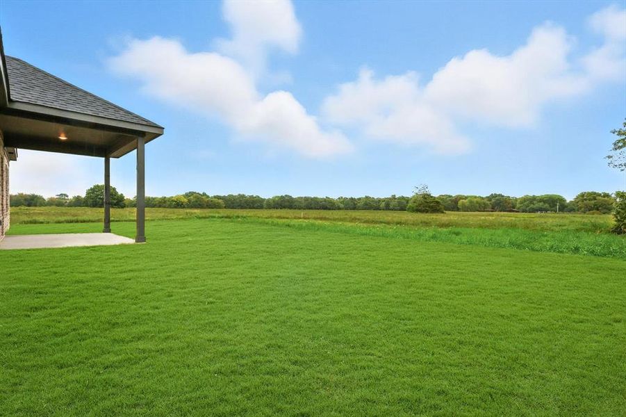 View of grassy yard featuring a rural view and a patio View of grassy yard featuring a rural view and a patio