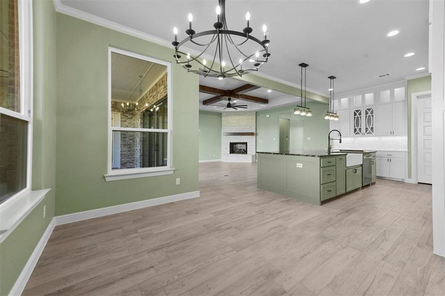 Kitchen with a large fireplace, decorative light fixtures, light hardwood / wood-style flooring, white cabinetry, and an island with sink