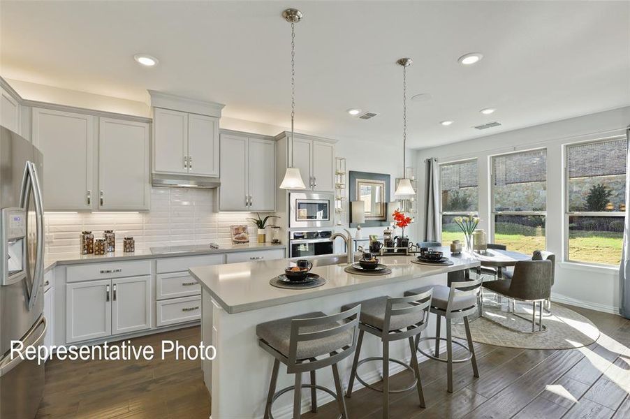 Spacious kitchen featuring white cabinetry, stainless steel appliances, a center island with pendant lighting, wood-finish flooring, and ample natural light from multiple windows