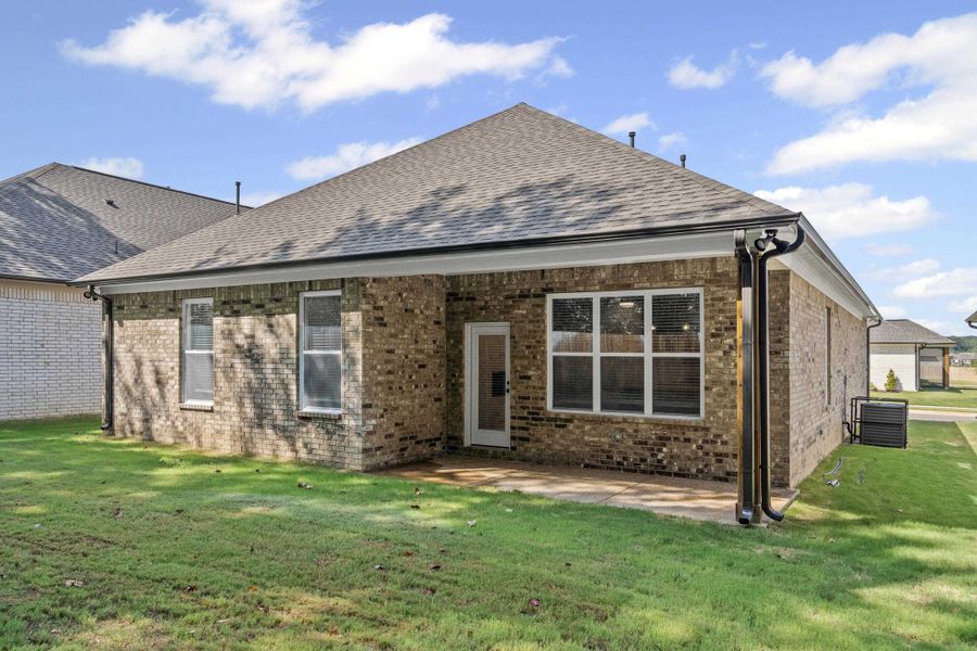 Back of house with brick siding, a yard, roof with shingles, and a patio