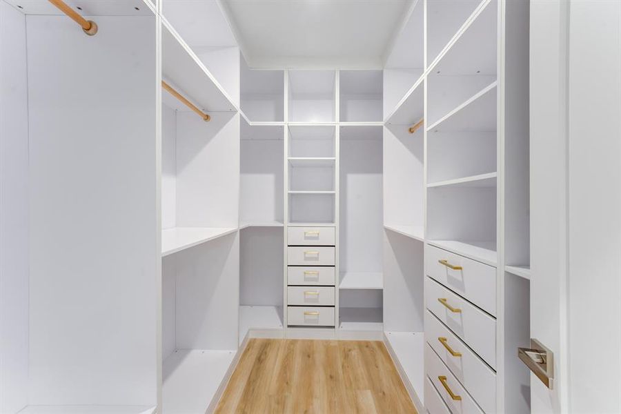 This large custom built closet features built-in drawers with gold accented hardware, storage space, and clothes hanging rods.