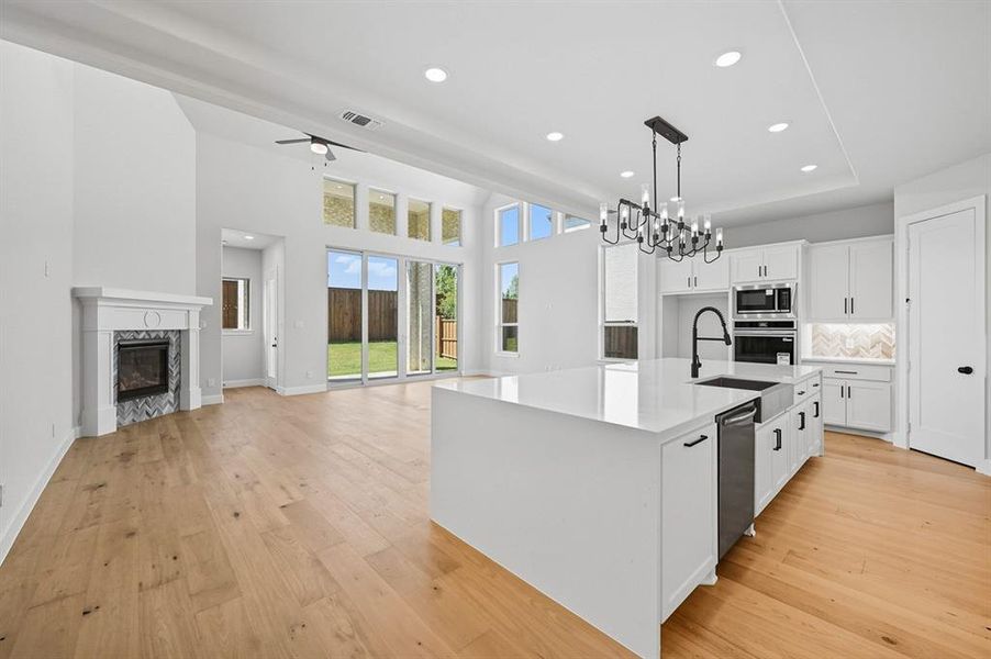 Kitchen featuring white cabinets, recessed lighting, a kitchen island with sink, tasteful backsplash, and a premium fireplace