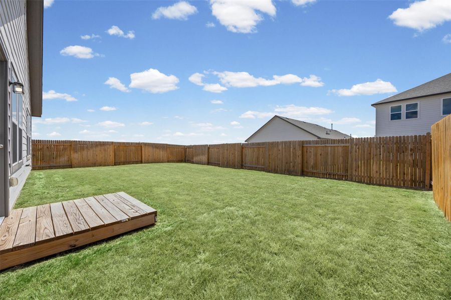 An expansive grassy yard is completely enclosed by a tall wooden privacy fence. An expansive grassy yard is completely enclosed by a tall wooden privacy fence.