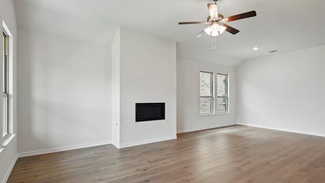 Spacious room featuring wood-finish flooring, a contemporary fireplace, multiple windows, a ceiling fan, and recessed lighting